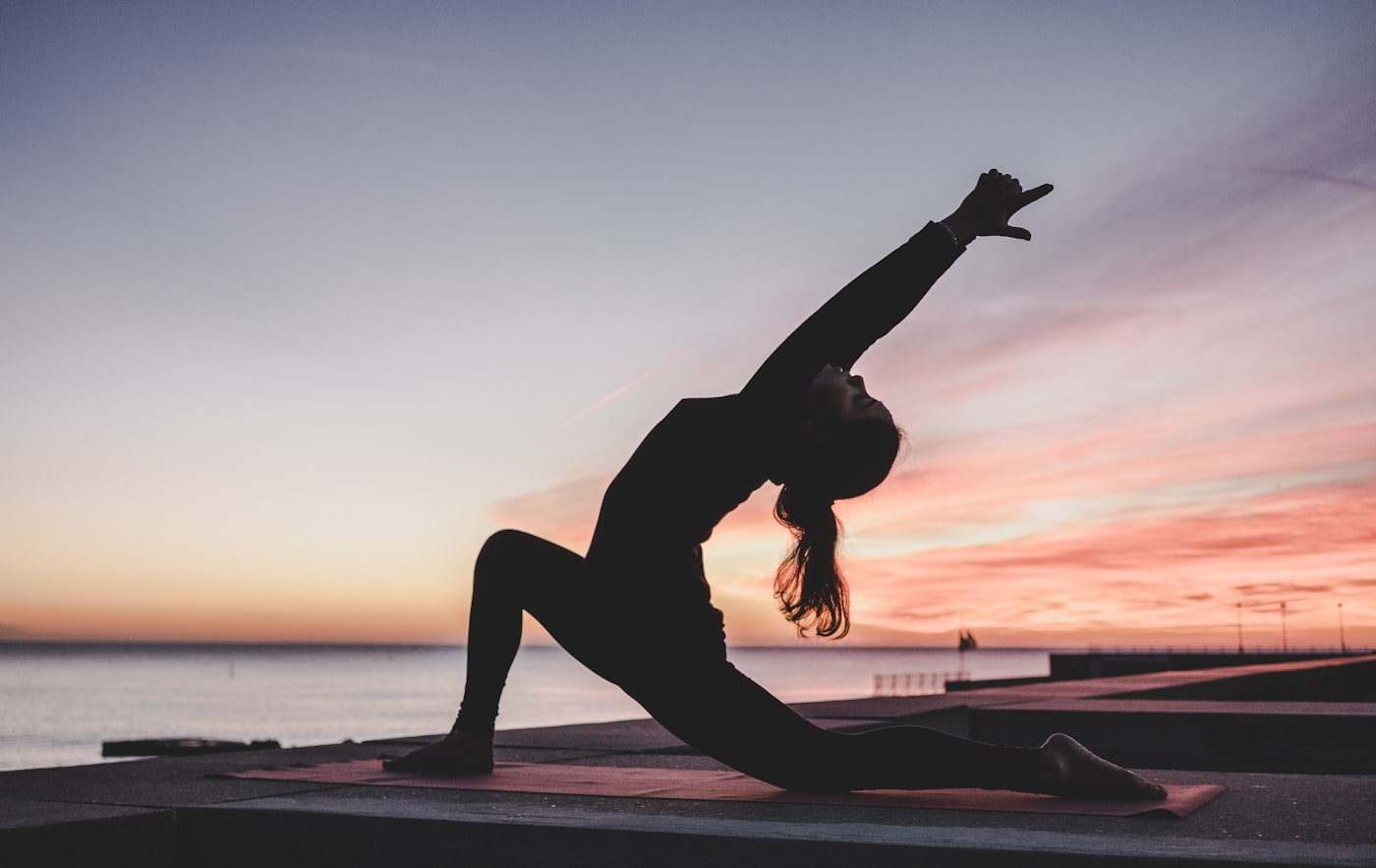 Silueta practicando yoga frente al mar al atardecer